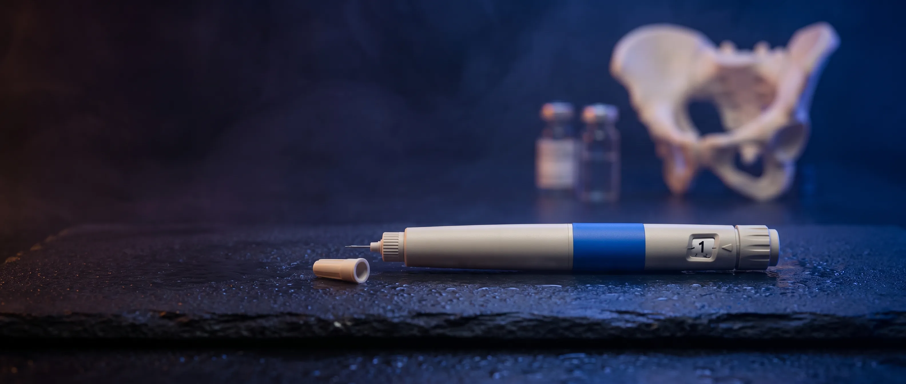 GLP-1 injection pen on wet slate with a blurred pelvis bone model behind it